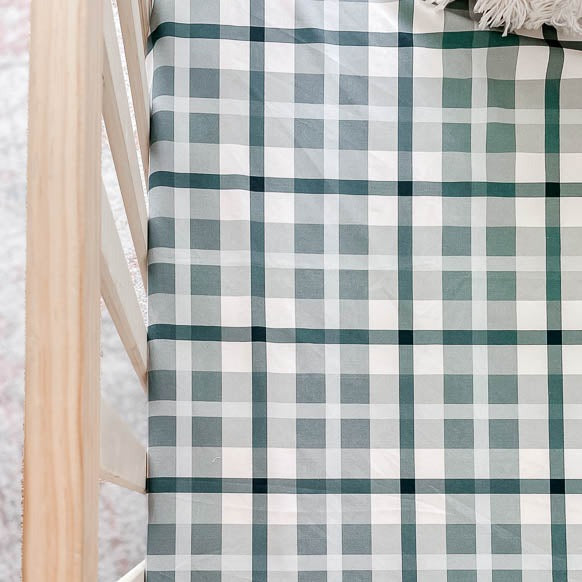 a close shot of a pine crib set with a blue plaid fitted crib sheet