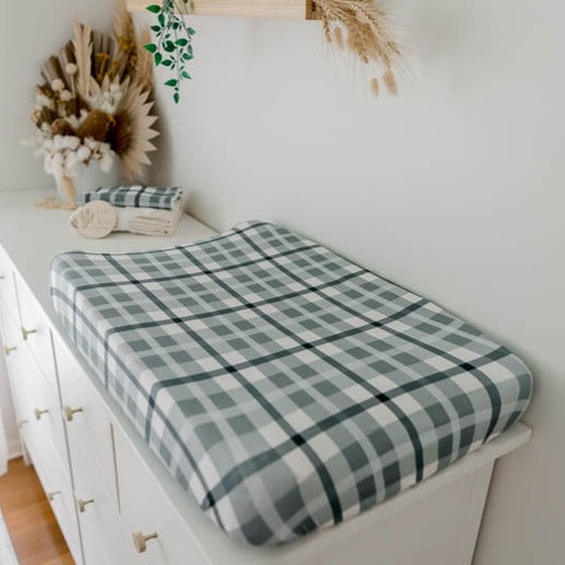 Blue plaid cotton bassinet sheet set out on a white pine chest of draws with a matching burp cloth in the background