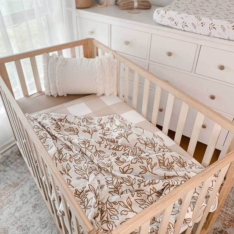 Baby Nursery with wooden crib and an Snuggly Jacks Foliage Sand Reversible Organic Knitted Blanket on the crib mattress