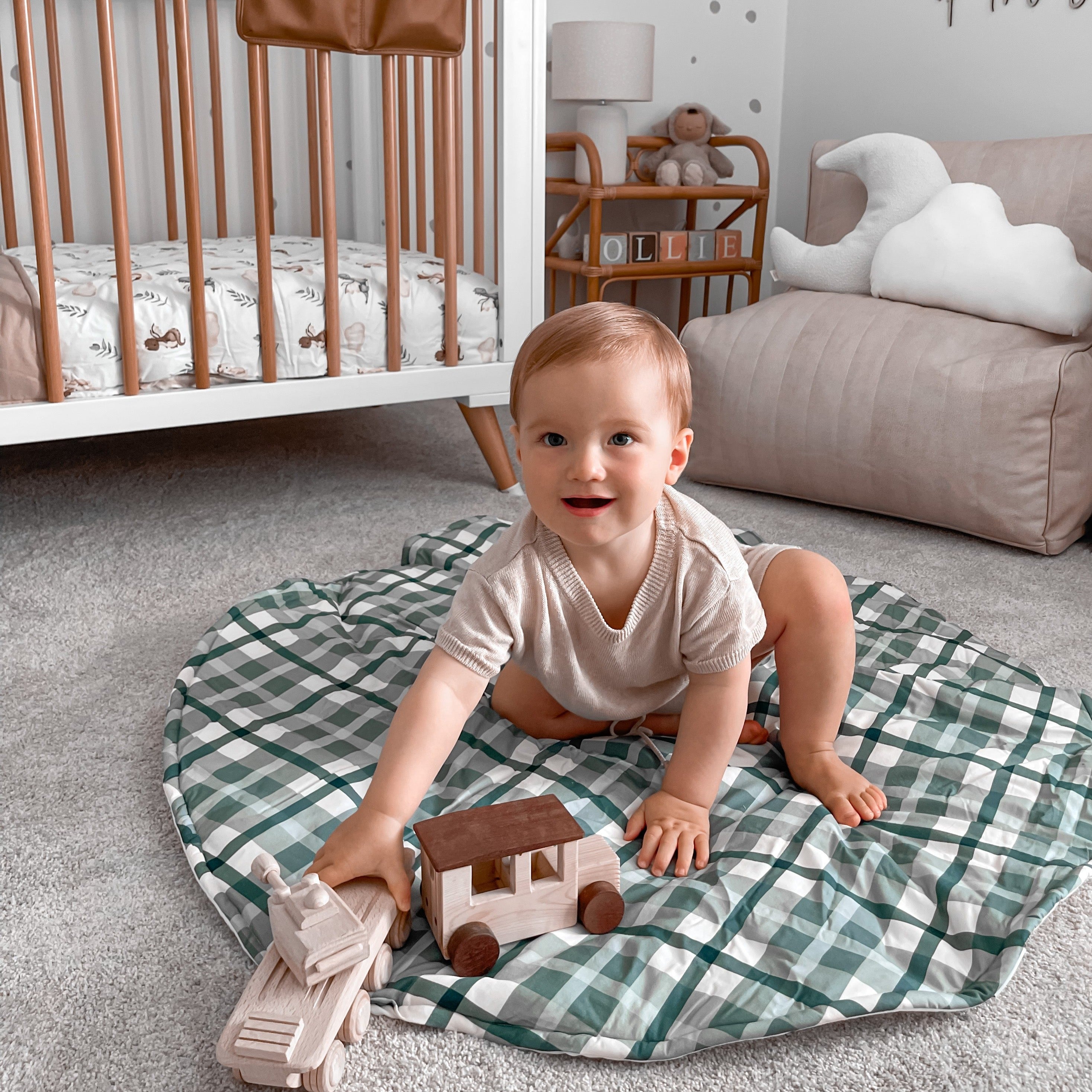 Little boy sitting on a blue cyprus plaid playmat playing with his toys in the middle a stylish nursery