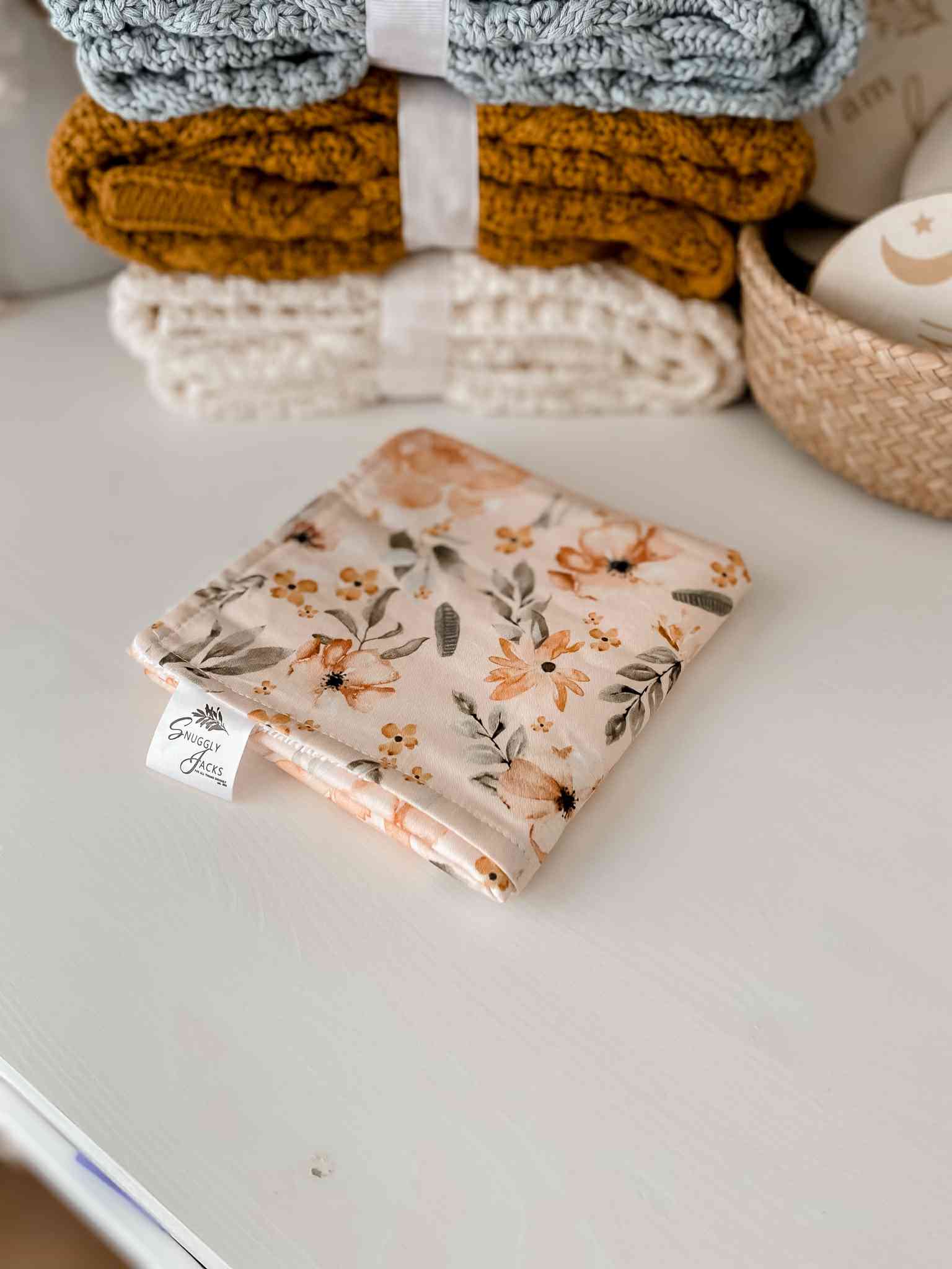 Honey, Cream and Cornflower Blue Knitted Blankets beside a Burp cloth with a soft floral print located in Canada