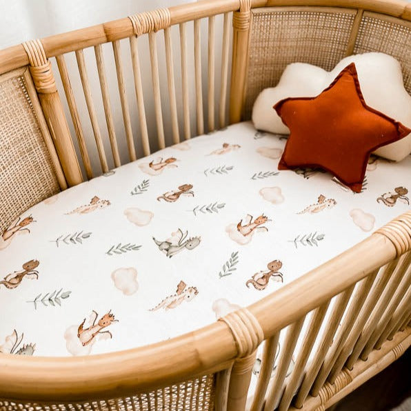 Close up of a white bassinet sheet with dragons, leaves and clouds on it in a stylish pattern