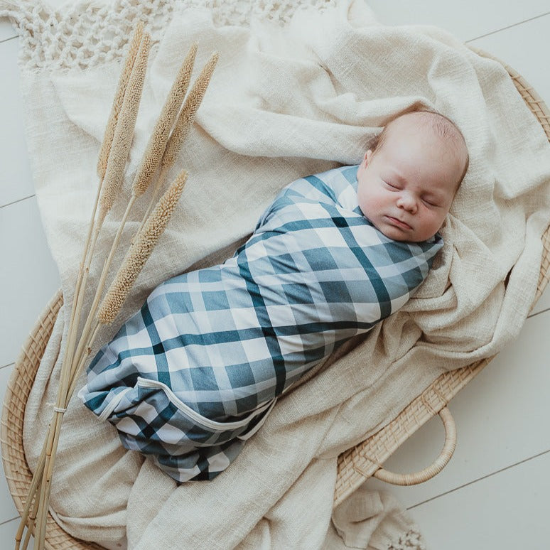 Adorable baby wrapped in a blue plaid wrap laying on top of a cotton blanket in a moses basket
