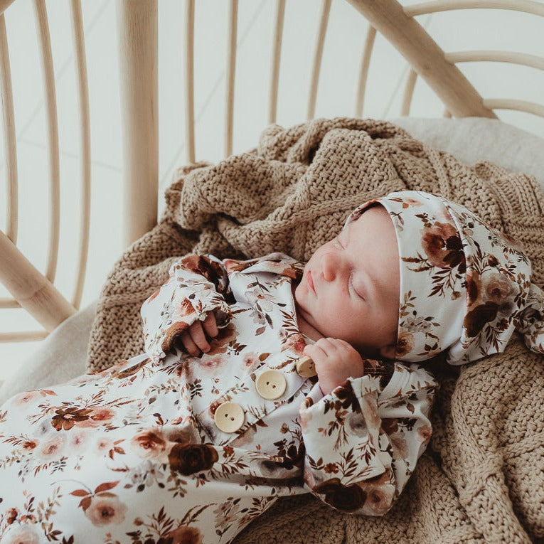 Close image of a baby sleeping in a bassinet with a cotton beanie and knotted gown keeping him snug