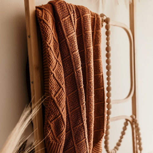 Wooden rattan ladder with a snuggly jack knitted blanket hanging over the rail