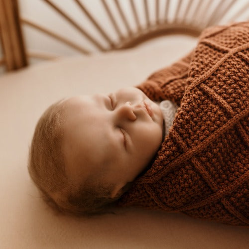 newborn baby laying in a rattan bassinet wrapped in a snuggly jacks organic knitted blanket