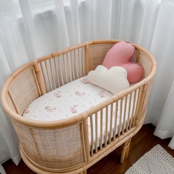 Soft white cotton bassinet sheet with swans in a rattan bassinet.
