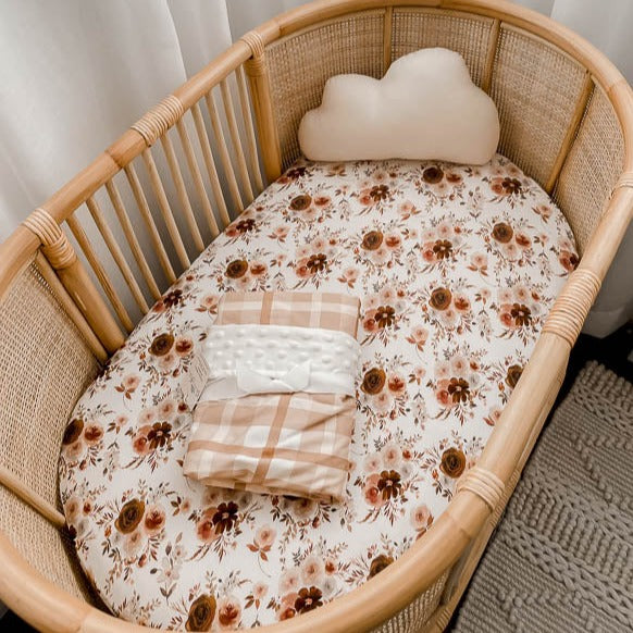 Cotton Bassinet cover with a warm brown and soft pink floral pattern in a rattan bassinet. 
