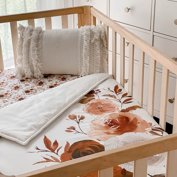 Pine crib from an angel showcasing a large print floral cotton quilt with a tasselled pillow resting in the corner