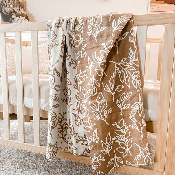 Baby Nursery with wooden crib and an Snuggly Jacks Foliage Sand Reversible Organic Knitted Blanket draped over the side of the crib